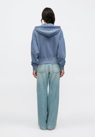 Ανοιχτό μπλε κοντό φούτερ με κουκούλα και κορδονάκι, με ριμπ μανσέτες, σε συνδυασμό με φαρδιά, ξεβαμμένα τζιν σε ανοιχτό μπλε διαβάθμιση.