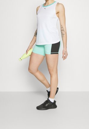 Canottiera sportiva bianca con dettagli turchesi, abbinata a pantaloni corti color acquamarina e neri. Sneakers nere e una bottiglia d'acqua gialla completano l'outfit.