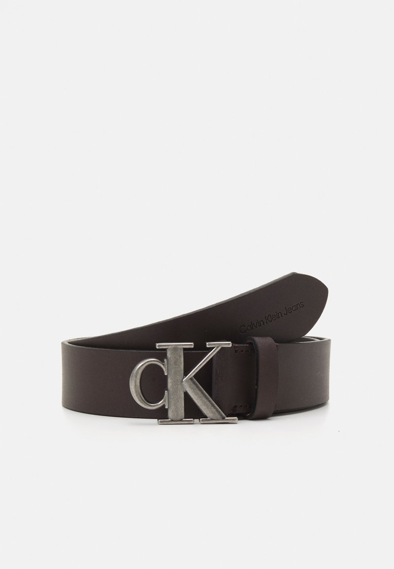 Barna bőr öv ezüst színű "CK" logós csattal, sima textúrával és klasszikus dizájnnal. Diszkrét márkázás a belső oldalon.