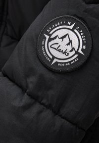 Czarna puchowa kurtka ze szczegółami w postaci okrągłej, czarno-białej naszywki Clarks z górami i współrzędnymi, teksturowana tkanina oraz pikowany wzór.