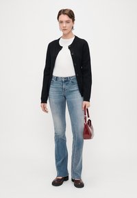 Μαύρο ζακέτα με στρογγυλή λαιμόκοψη και κλείσιμο με κουμπιά, λευκό τοπ, ανοιχτό μπλε φουσκωτά τζιν, καφέ πλατφόρμες και κόκκινη τσάντα.