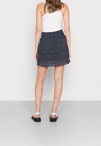 Navy blue patterned skort with a ruffled tier at the hem, made of lightweight fabric. Paired with white sandals, showcasing a casual look.