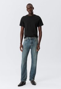 Black short-sleeve t-shirt paired with light blue straight-leg jeans. The jeans feature a faded wash and classic five-pocket design. Black leather boots.