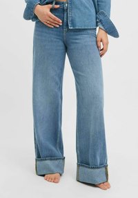 Jeans de pierna ancha de color azul claro con los puños enrollados, fabricados en denim. Presentan una cintura alta y una textura suave. Sin patrones o adornos visibles.