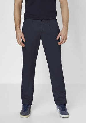 Navy stretchy chinos with a slim fit, featuring pockets and a button closure, paired with dark sneakers on a neutral background.