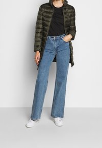 Padded olive green coat with high collar, paired with blue wide-leg jeans and white sneakers, featuring a simple design and soft texture.