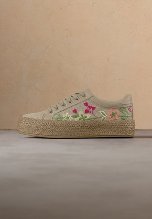 Deportiva de plataforma beige con suela tejida y diseños florales bordados en rosa, verde y blanco en el lateral, exhibida sobre una superficie gris.