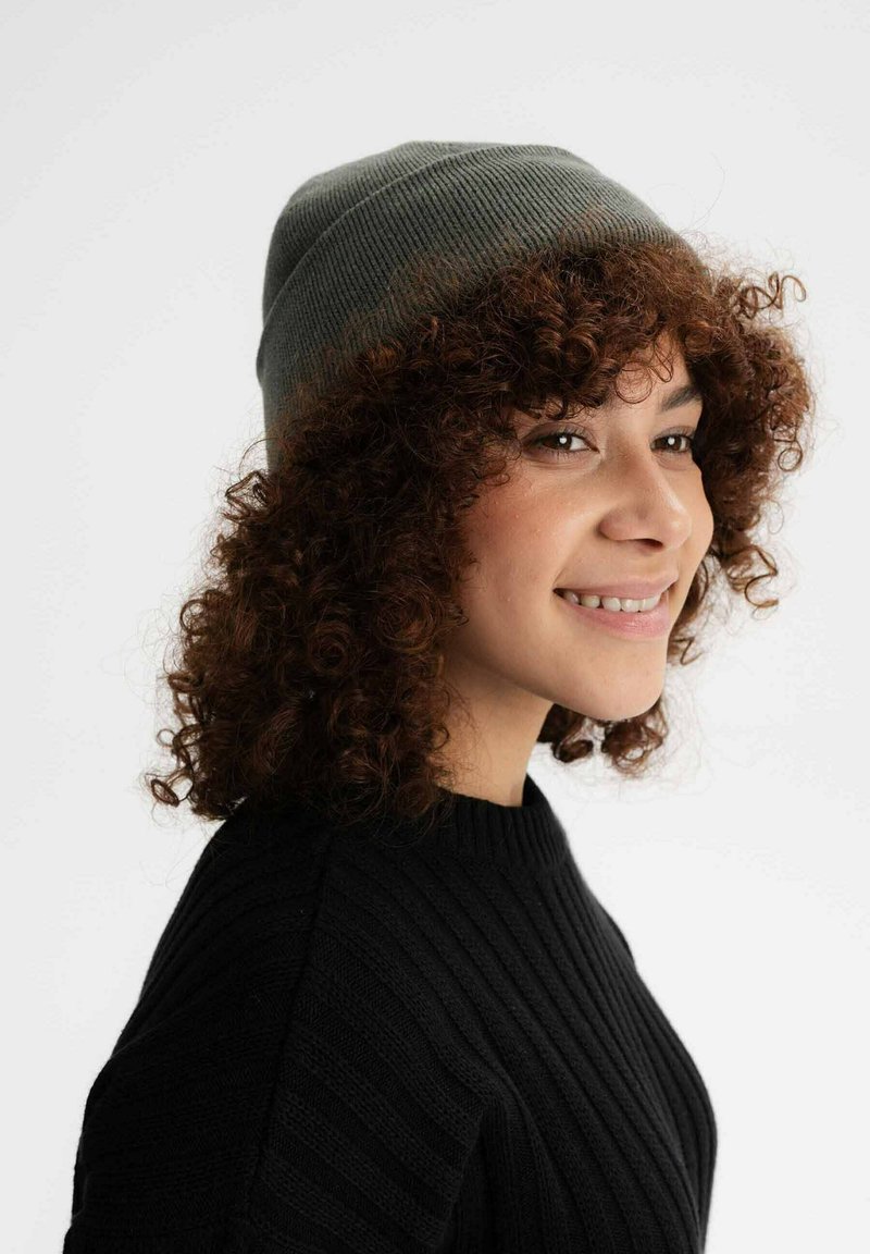 Grijze gebreide beanie met ribbeltextuur, snug op een krullend kapsel, contrasterend met een zwarte ribbeltrui.