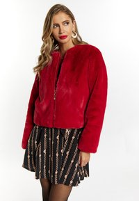 Jachetă roșie din blană sintetică cu închidere cu fermoar, design scurt și mâneci lungi. Asortată cu o fustă neagră cu modele din lanțuri aurii.