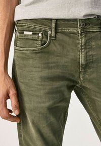 I jeans in denim verde oliva presentano un classico design a cinque tasche, un tessuto testurizzato, un leggero effetto di scoloritura e dettagli in hardware tono argento.