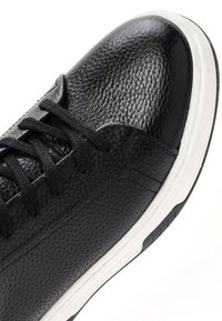 Sneaker in pelle nera texturizzata con lacci neri e suola in gomma bianca, mostrato da una vista ravvicinata angolata dall'alto.