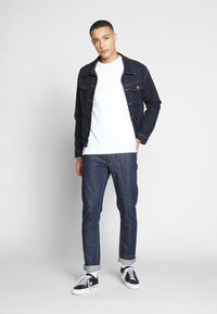 Jachetă din denim de culoare albastru închis, tricou alb și blugi negri cu manșete răsucite. Adidași alb-negru completează ținuta.