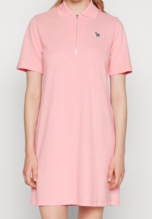 Femme portant une robe polo rose à manches courtes avec une fermeture éclair devant et un petit logo zèbre sur la poitrine gauche.