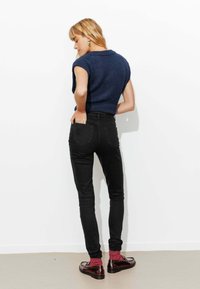 Haut en tricot à manches courtes marine, jean skinny taille haute noir, chaussettes bordeaux et mocassins marron. Design simple sur fond blanc.