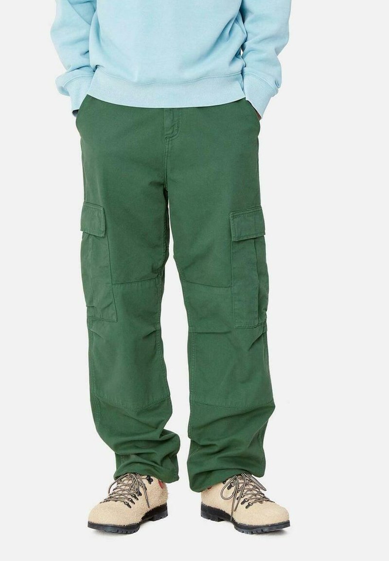 Groene cargobroek met meerdere zijzakken, een relaxed fit en gemaakt van duurzaam materiaal. Gecombineerd met lichtbruine schoenen.