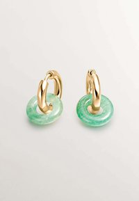 Los pendientes de aro de oro presentan un acento circular verde translúcido con una textura suave. El oro añade un elemento metálico contrastante.