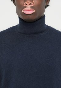 Mornarsko turtleneck z mehkega volne z gladko teksturo. Ima prilegajoč silhueto in rebrast ovratnik, primeren za plastenje.