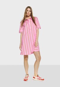 Růžové šaty s krátkým rukávem a bílými a červenými svislými pruhy, s knoflíkovou léga vpředu a volným střihem. Nosené s barevnými teniskami.