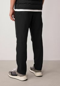 Black athletic pants with a fitted design, featuring a zippered pocket and reinforced seams, paired with gray and white sneakers.