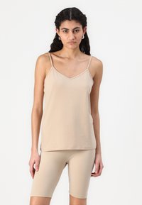 Beige tank top, mille õhukeste rihmadega ja V-kaelusega, koos sobivate fikseeritud lühikeste pükstega. Mõlemad on valmistatud pehmest ja elastsemast kangast.