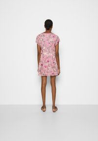 Kort rosa blommig klänning med korta ärmar, med en lös passform och en subtil textur, visad bakifrån mot en neutral bakgrund.