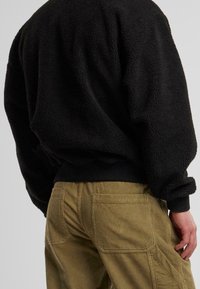 Sort fleece sweatshirt med en struktureret overflade og ribstrikkede manchetter, parret med olivengrønne kordfløjlsbukser med flere lommer og en diskret ribbning.