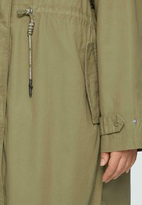 Olijfgroene parka-jack met een trekkoord in de taille, drukknoopmanchetten en een zijzak. De stof heeft een gladde, duurzame textuur.