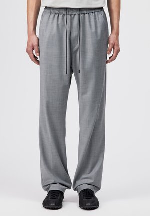 Mand iført løstsiddende lysegrå bukser med elastisk talje og sorte snore, kombineret med sorte sneakers.