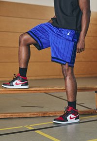 Élénk kék Nike kosárlabda rövidnadrág függőleges csíkokkal és fekete részletekkel, fekete és piros magasszárú tornacipővel párosítva.