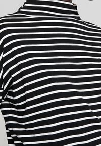 Mustapohjainen turtleneck-paita, joka on valmistettu pehmeästä kankaasta, jossa on vaakasuoria raitoja eri leveydellä ja tiukka kaula-aukko.