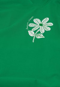 Groene katoenen t-shirt met een wit bloemenontwerp, inclusief bladeren en tekst. De stof heeft een gladde textuur en een ronde halslijn.