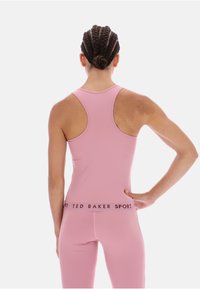 Roza atletska majica brez rokavov z dirkaškim hrbtom, ki se ponaša z gladko teksturo in blagovno znamko na elastičnem pasu.
