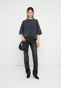 Mörkgrå oversized tröja, svarta jeans, håller en svart hobo-väska. Outfiten har en avslappnad passform och eleganta texturer.