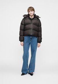 Chaqueta de plumas negra con un diseño corto, que presenta una capucha y cierre de cremallera. Combinada con vaqueros de pierna ancha de color azul claro y zapatos negros de punta.