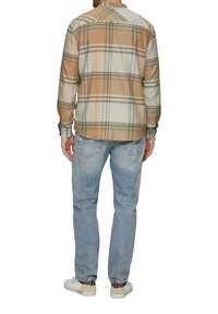 Beige geruite overhemd met groene en blauwe lijnen, knoopdetails bij de manchetten, gecombineerd met lichtblauwe jeans en witte sneakers.