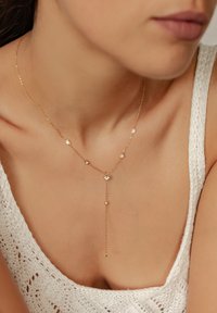 Goldene Kettenhalskette mit klaren Edelsteinen in unterschiedlichen Größen, einschließlich eines Tropfenanhänger-Designs, vor einem hellen Hintergrund präsentiert.