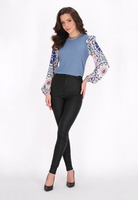 Top blu ribbed con maniche lunghe a fantasia blu, rosa e bianco, abbinato a pantaloni neri aderenti e tacchi alti neri.