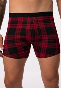 Boxer-culottes à carreaux rouges et noirs avec un tissu doux, une taille élastique arborant le logo "JP1880" et un design ajusté.