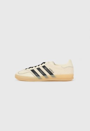 Baskets Adidas Gazelle crème et noires avec semelle en gomme, bandes latérales et dessus tissé texturé, vues de côté extérieur sur fond blanc.