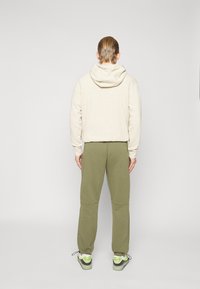 Beige hoodie med snörning och texturerad tyg, i kombination med olivgröna sweatpants med avslappnad passform och ribbade manchetter och nederkant.