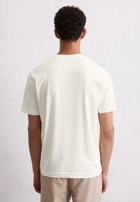 Hellbeige T-Shirt mit kurzen Ärmeln aus weichem Stoff, ausgestattet mit einem klassischen Rundhalsausschnitt und einem einfachen, schlichten Design.