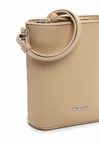 Beige läderhandväska med texturerad yta, rund topphandtag och dragkedja. Har en silverfärgad logotypdetalj på framsidan.