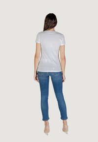 T-shirt bianco a maniche corte, design aderente, tessuto morbido, abbinato a jeans skinny blu e scarpe con il tacco trasparenti color nude.