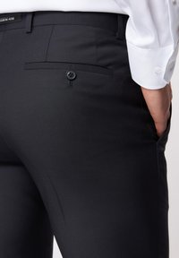 Czarne dopasowane spodnie uszyte z gładkiego materiału, z jedną tylną kieszenią na guzik. Projekt charakteryzuje się subtelną fakturą i slim fit.