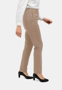 Beige op maat gemaakte broek met een elastische tailleband, taps toelopende pasvorm en een gladde textuur, gecombineerd met zwarte hoge hakken.