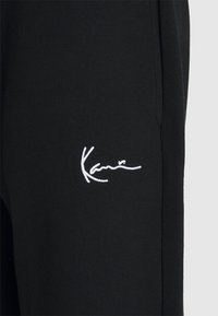 Black sweatpants made of soft cotton with a slim fit, featuring white embroidered logo detailing on the left thigh.