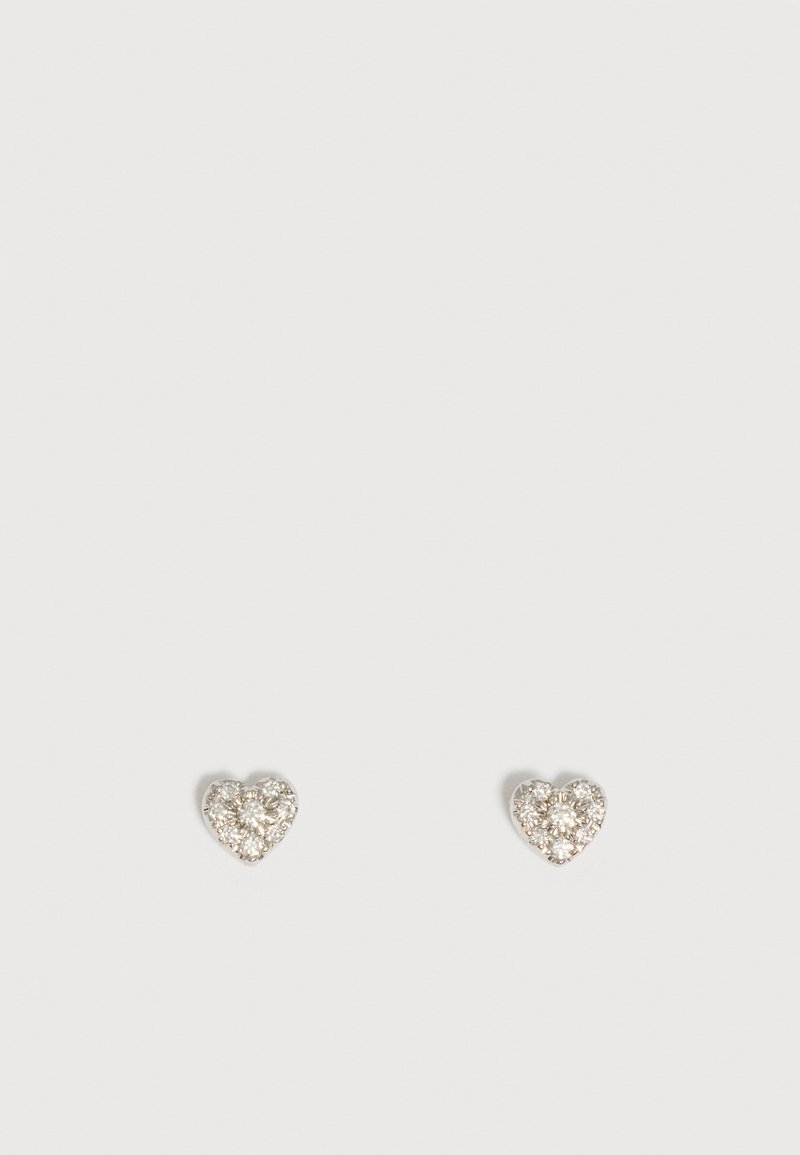 Paire de petites boucles d’oreilles en forme de cœur serties de pierres claires et scintillantes sur un fond clair uni.