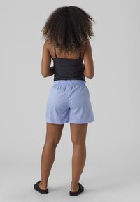 Shorts bleu clair à rayures avec une ceinture élastique, assortis d'un débardeur noir, vus de dos. Sandales noires aux pieds.