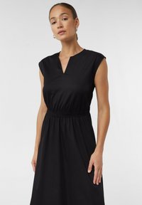 Czarna sukienka bez rękawów z dekoltem w serek, elastyczną talią i zwiewnym dołem. Wykonana z gładkiego materiału o prostym, minimalistycznym wzorze.