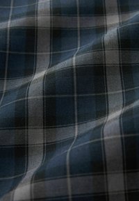 Gros plan d’un tissu à carreaux bleu foncé et gris avec de fines lignes blanches et une texture légèrement froissée.